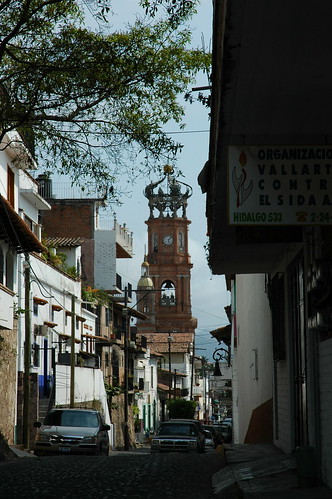 Cathedral of Our Lady of Guadalupe, Calvario, looking down an alleyway, to the east, bell tower, clock, crown of angels, trees, houses, Puerto Vallarta, Jalisco, Mexico by Wonderlane
