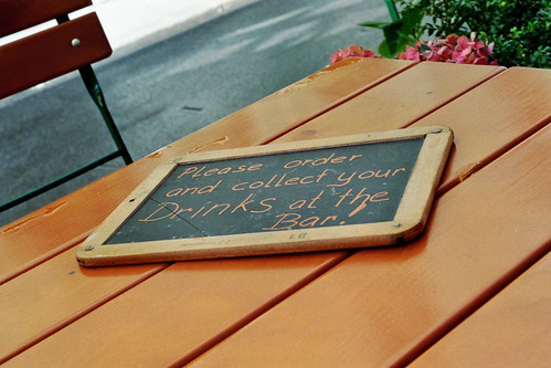 Photo handgeschriebenes Schild 'Collect your drinks at the bar' auf Holztisch