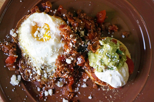 Masa harina biscuits with spicy chorizo topping, seen from overhead: the sunlight glistens on the yolk of a fried egg, and the white cotija stands out boldly against the chorizo and guacamole
