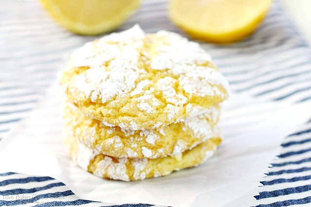 Lemon Crinkle Cookies stacked up on parchment paper with a sliced lemon.