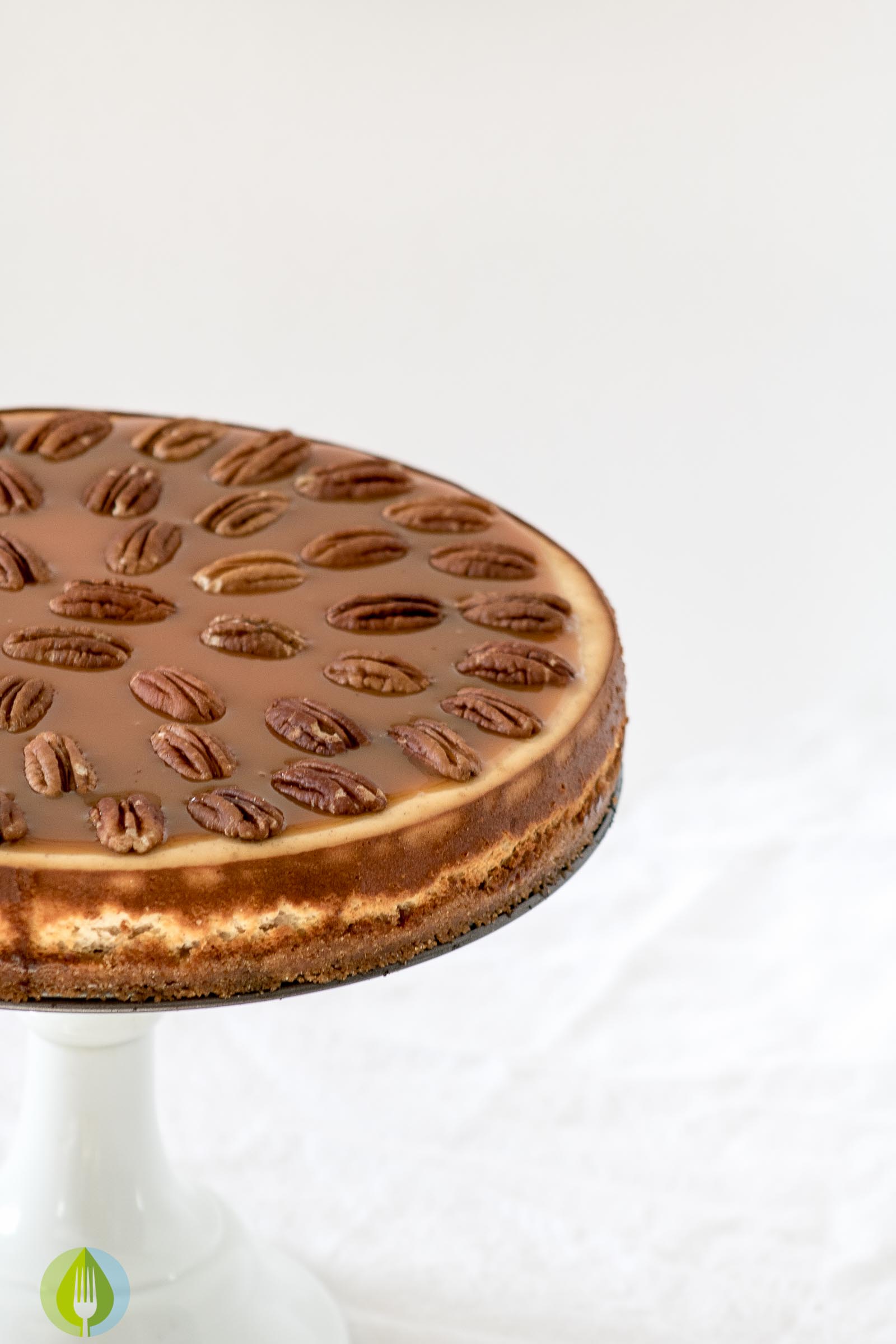 Canadian Whiskey cheesecake on a cake stand, cake is overed in pecans and caramel sauce