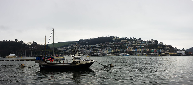 A solitary fishing boat is framed in harvour with colourful rows of houses on the hill behind.