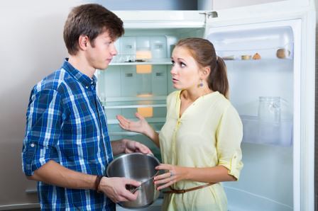 Upset hungry couple standing near empty shelves of fridge