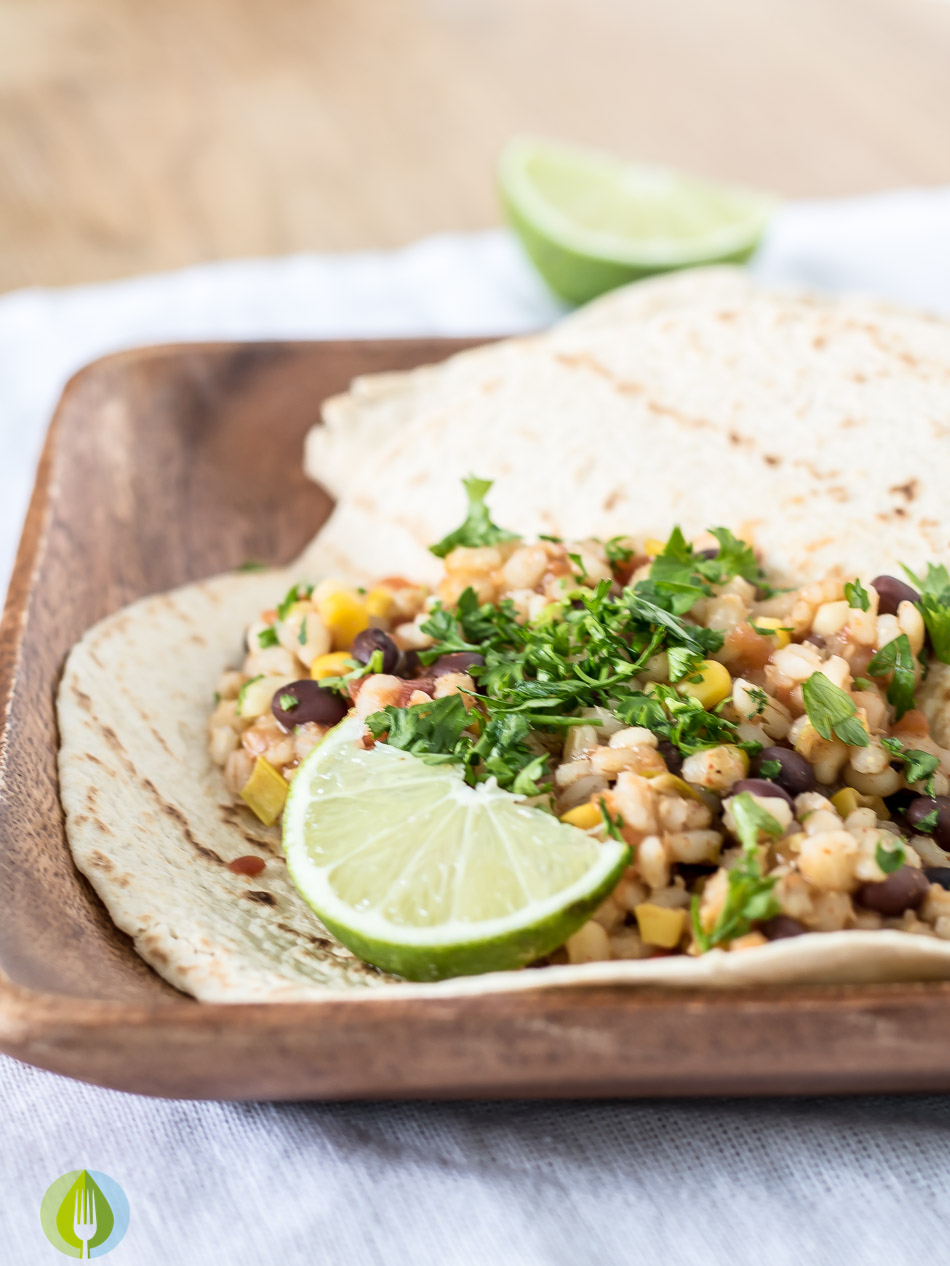 whole grain torilla filled with black bean and barley burrito filling with lime on a wood plate