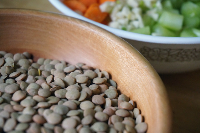 Close-up of brown lentils in a wooden bowl, countless convex grey-brown shapes mounded on each other