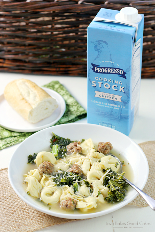 Italian Tortellini Soup in a bowl with a spoon and a bread roll on a plate next to a carton of Progresso Cooking Stock.