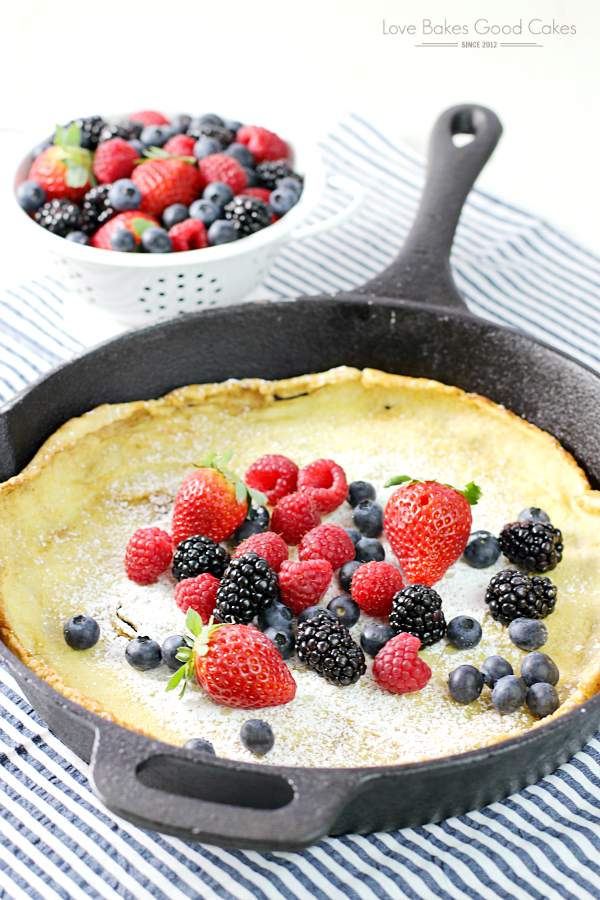 Dutch Baby Pancake with Fresh Berries in a skillet with a bowl of fresh berries.