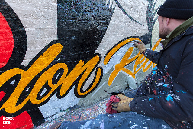 British street artist D*Face painting a mural with brushes and paint in Shoreditch, London