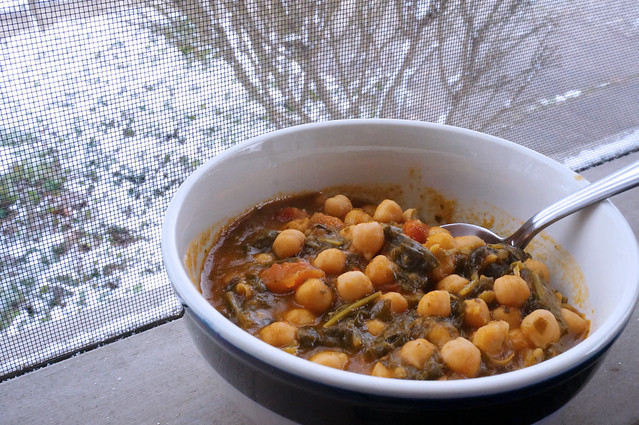 A bowl of chickpea stew sits on a porch rail. In the background we see my yard, ivy and bushes all covered in snow.