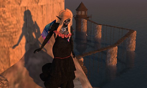 Image Description: Full body shot of a woman looking down out of frame; behind her is a staircase up nearby and a bridge in the distance to a pillar over the water behind her.