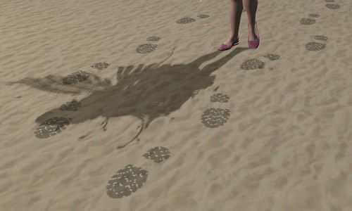 A sandscape with two sets of booted footprints. Much smaller feet in flats decorated in a heart cast a shadow over the footprints.