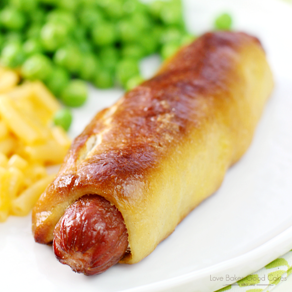 Easy Pretzel Dog close up on a white plate with macaroni and cheese and green peas.
