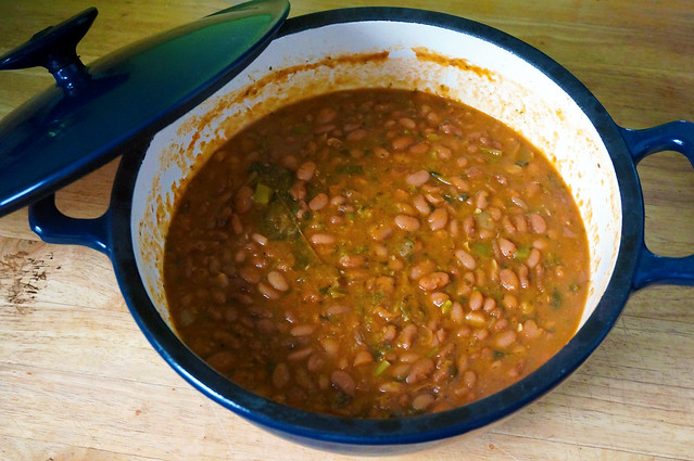Dominican beans, an orangey-pink stew inside an enameled cast iron Dutch oven. The beans contrast with the cream-colored interior, which itself stands out from the dark blue of the pot's exterior, and its lid leaning against it.