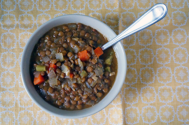 A bowl of basic lentil soup on a yellow napkin, a stainless steel buried deep in it. Bright-orange carrots punctuate the dark brown broth