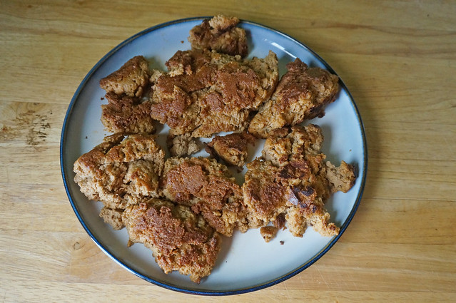 Pan-fried seitan, browned and crunchy, fills a white plate with a dark-blue rim, sitting on a wooden counter