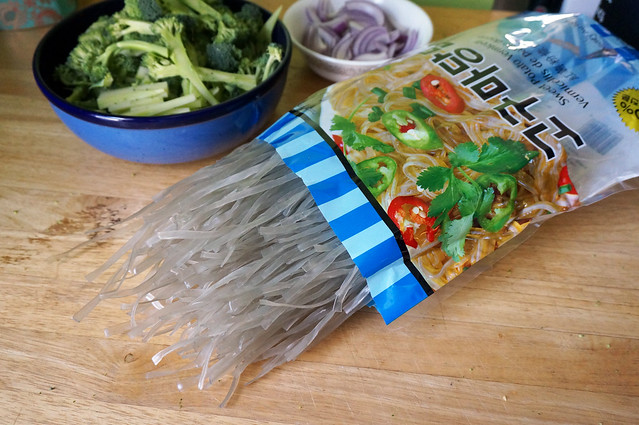 Grey, stiff noodles half-poured out of a brightly colored plastic bag -- the contrast between the drab noodles and the bright packaging is striking