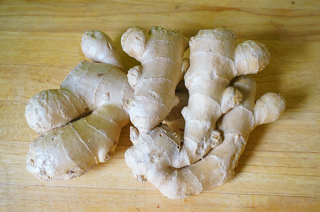 Two hands of unpeeled raw ginger rest atop each other on a wooden countertop