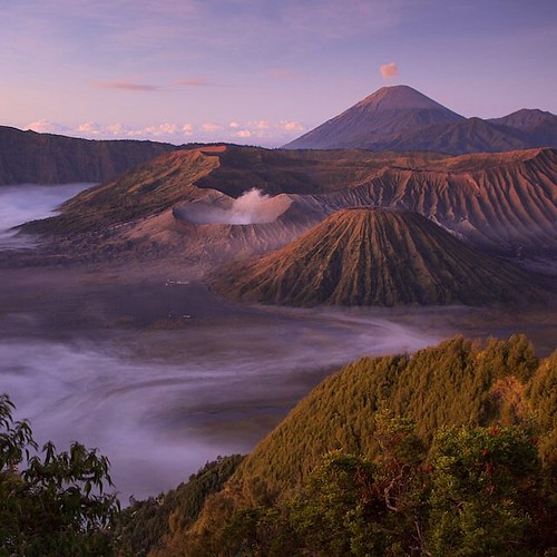 Photo by @TimLaman. A pre-sunrise glow hits the other-worldly landscape of the smoking Mount Bromo in the Tengger Caldera. In the background, Mount Semeru, the perfect shaped active volcano and the highest mountain in Java, has just let out a puff. #sunri