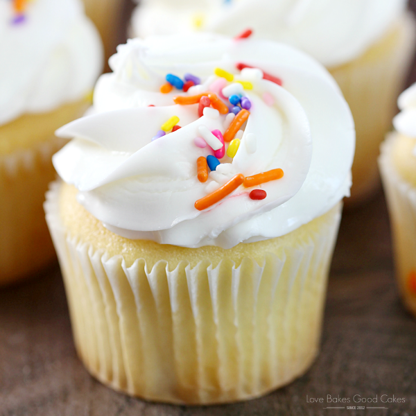 Bakery-Style Vanilla Cupcakes with white frosting and rainbow sprinkles close up.