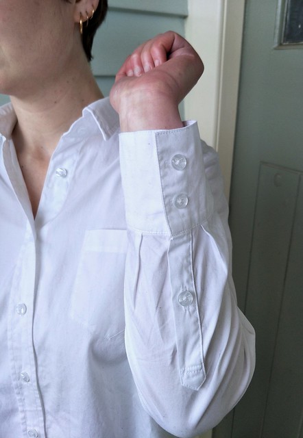 A woman wears a button up shirt and holds her arm to reveal a shirt cuff placket.
