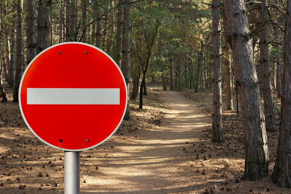 'do not enter' sign positioned in front of inviting wooded path