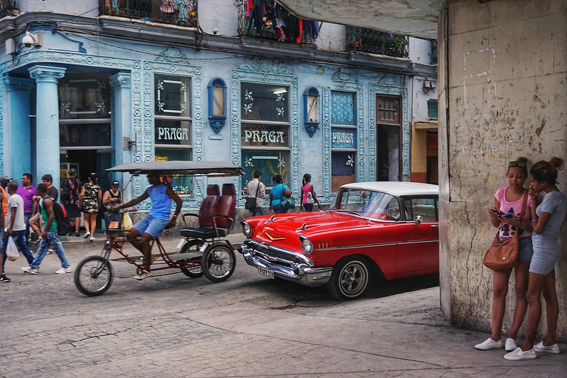 Girls on their phones and cars driving in a Havana street scene