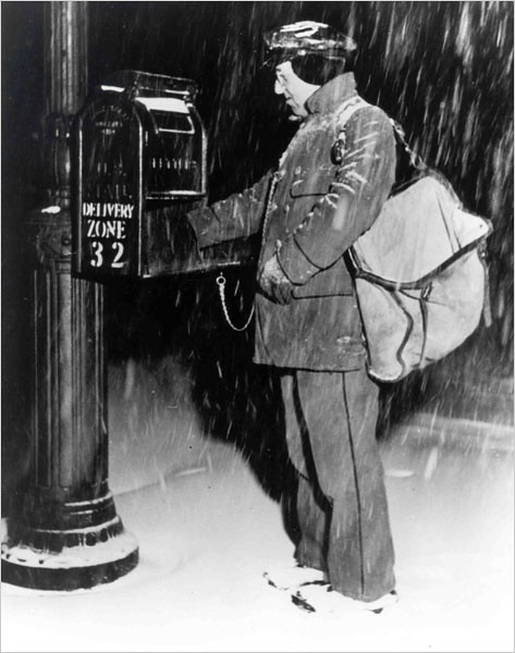 Uniformed city letter carrier removing mail from a mailbox in the snow.