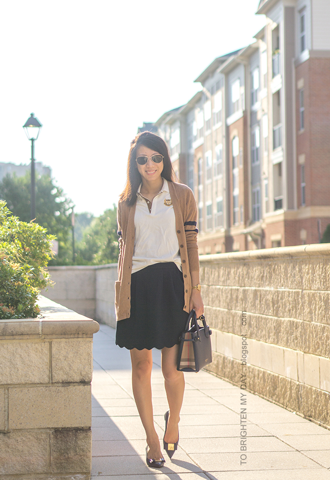 camel long varsity cardigan, polo with crest emblem, navy scallop skirt, gold watch, navy tote, navy bow pumps with block heel