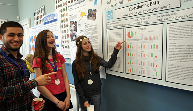 Two young people stand next to their poster talking to a visitor about their project