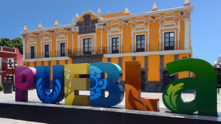 The name of the city spelled out in bright letters with a yellow building in the background in Puebla, a UNESCO Heritage site in Mexico