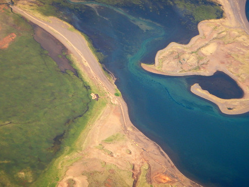 Aerial shot of where a turquoise river meets the ocean in Iceland from a commercial Icelandair flight