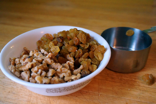 Chopped walnuts and golden raisins nestled against each other in a white ceramic bowl