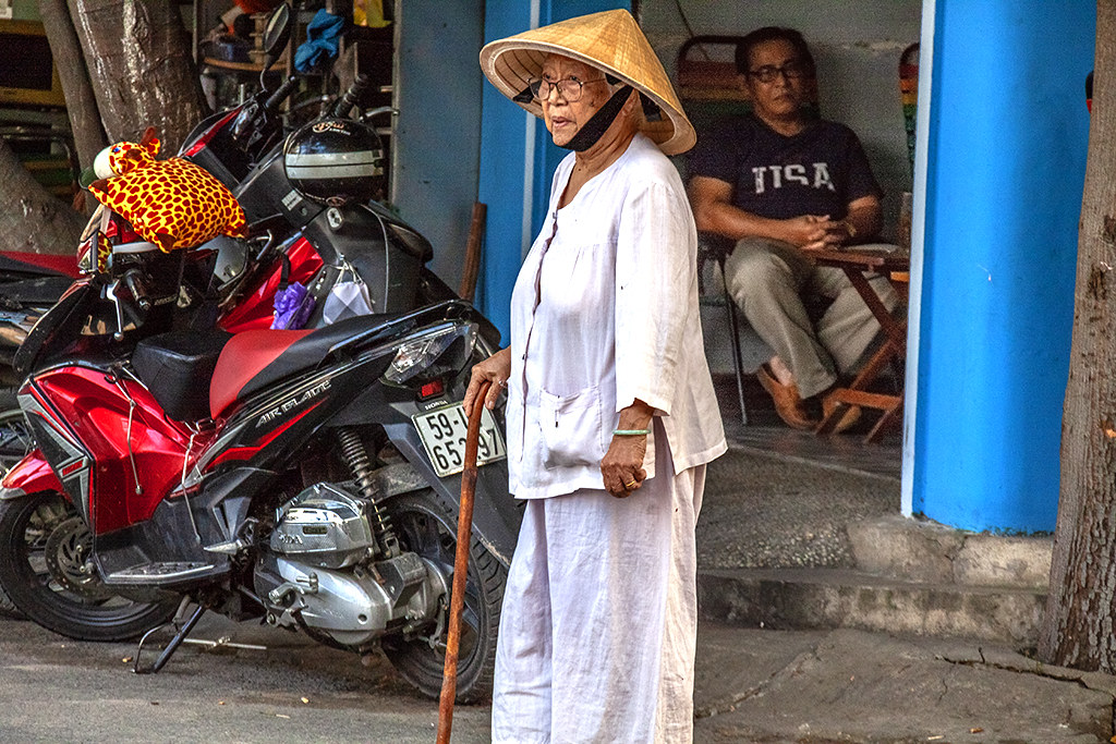 Old woman in conical hat and man in USA T-shirt--Saigon