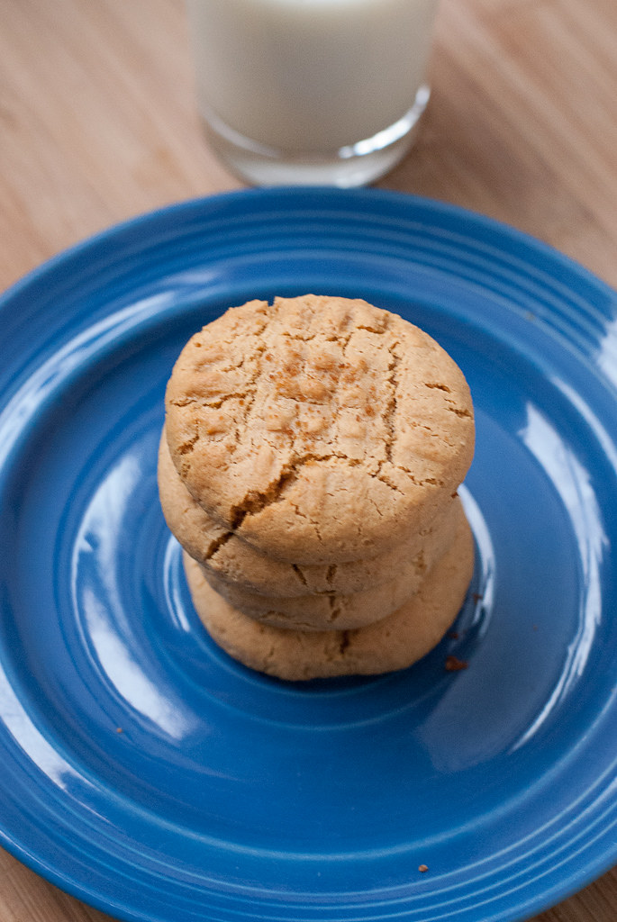 blue plate with tan peanut butter cookies stacked on top of it, glass of milk