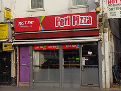 A ground-floor terraced shopfront with a large red sign above reading “Peri Pizza” and urging customers to download the Just Eat app.  The frontage is fully glazed, with frosted glass in the lower half.  A light purple door to the left bears numbering for “202 A B”.