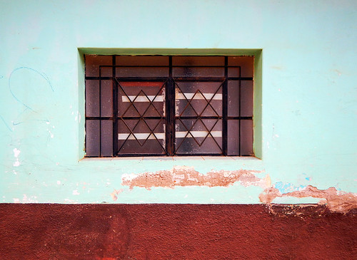 A barred window in a turquoise and dark red wall in Talpa, Mexico