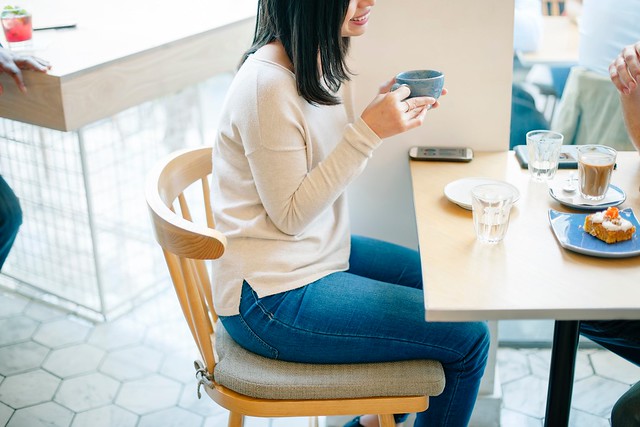 Image of woman sat at a table, drinking tea and eating cake