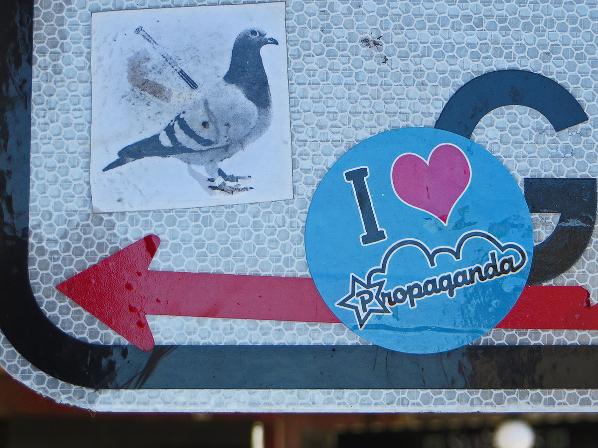 A picture of a sticker on a road sign. The sticker says I love propaganda